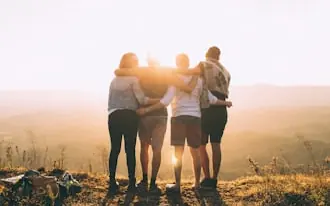 A group of friends standing together with arms around each other at sunset
